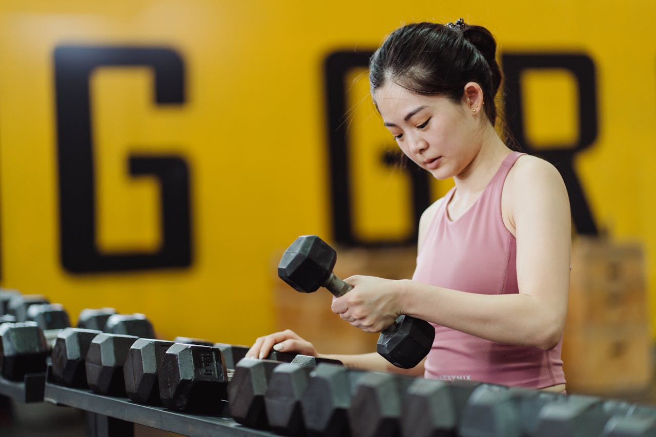 Young woman lifting dumbbell in gym, focusing on strength training with sports equipment.